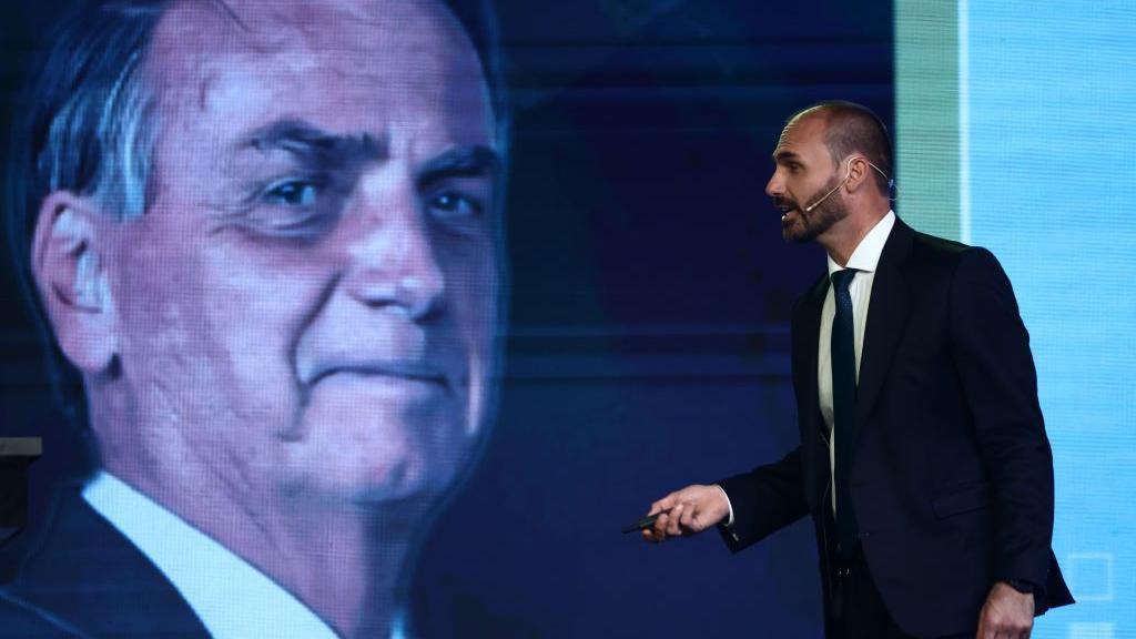 Eduardo Bolsonaro em frente a uma foto do pai, Jair Bolsonaro.