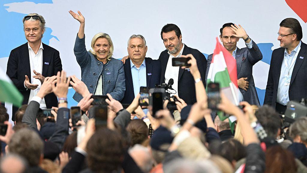 Viktor Orban stoji na pozornici između žene i muškraca okruženi fotografima i novinarima