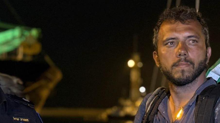 Thiago Avila com olhar confiante, observando algo em pé em área portuária à noite