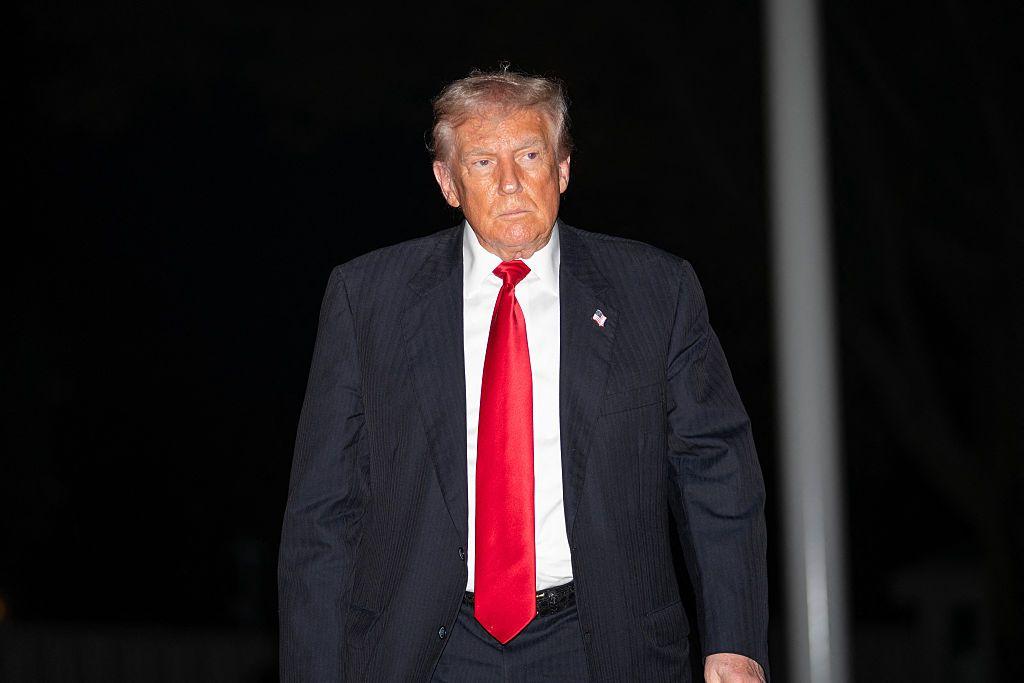 Donald Trump caminhando. Ele usa uma gravata vermelha e terno preto