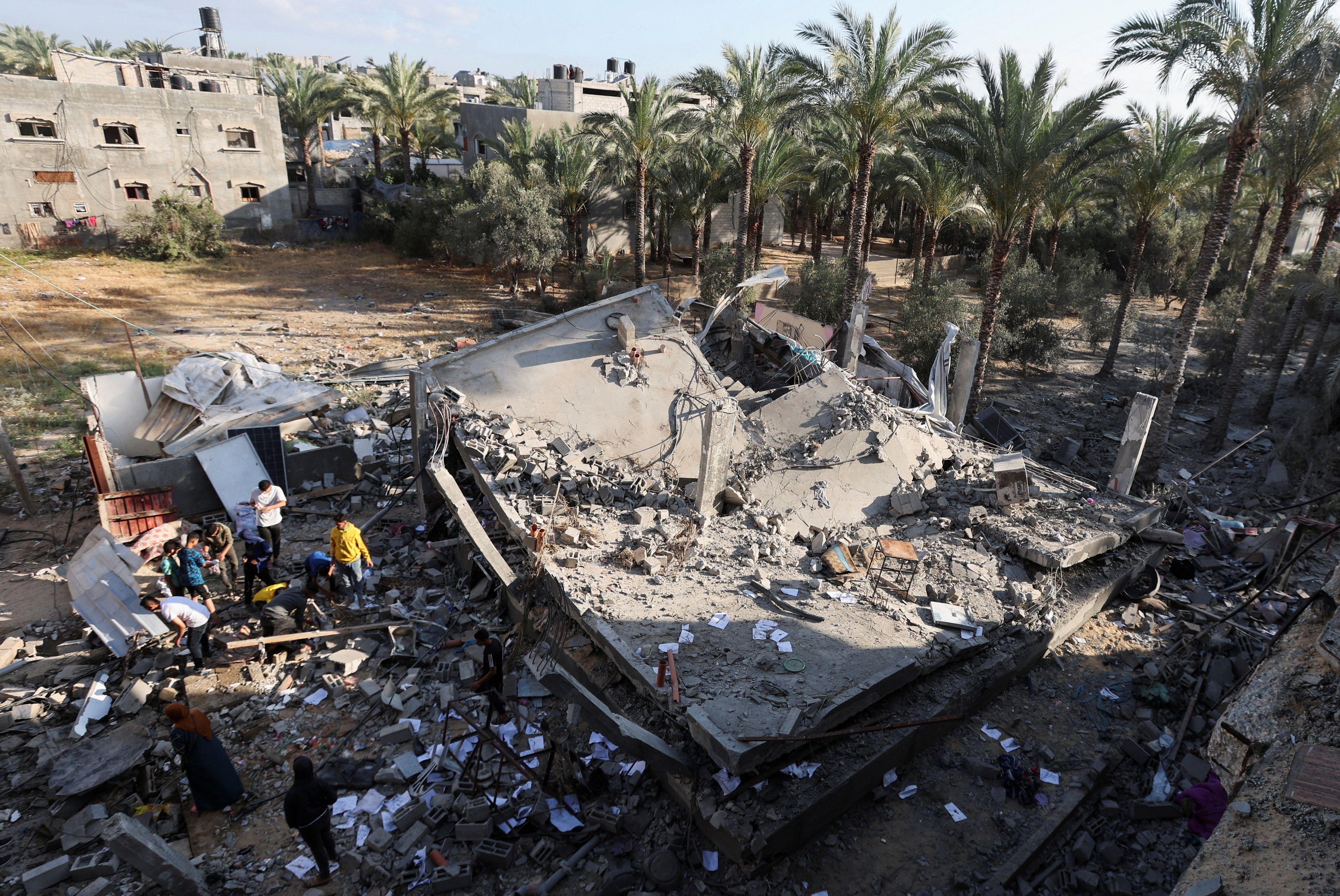 فلسطينيون يتفقدون الأضرار في موقع غارة إسرائيلية على منزل في دير البلح وسط قطاع غزة، 21 مايو/أيار 2025.