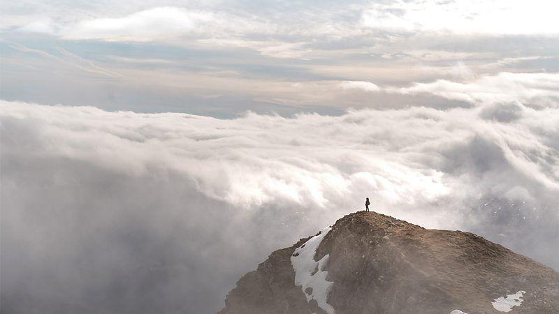 Pessoa sozinha no alto de uma montanha, com nuvens ao fundo