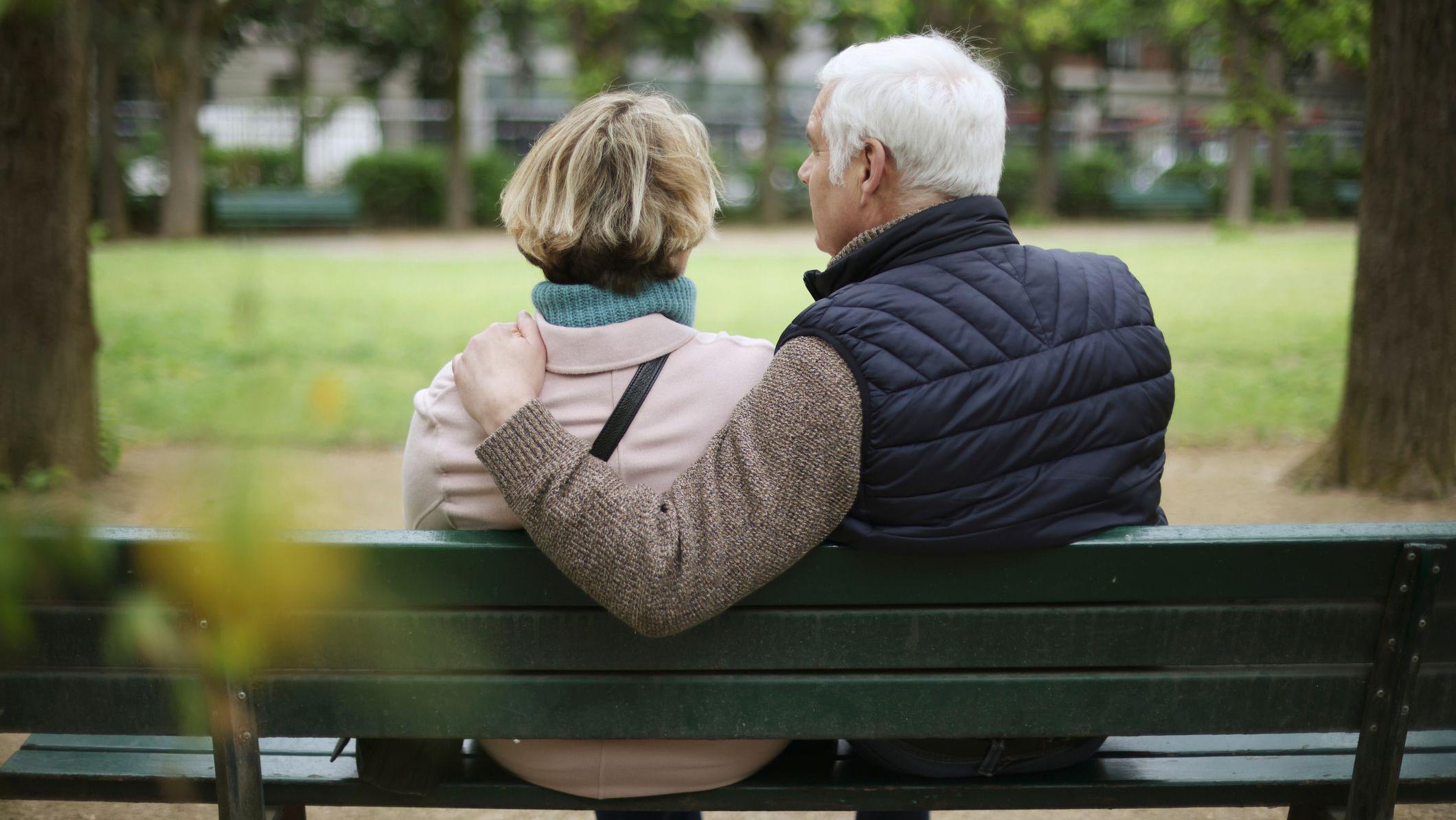 Casal de idosos sentado em um banco de parque, de costas para a c&acirc;mera
