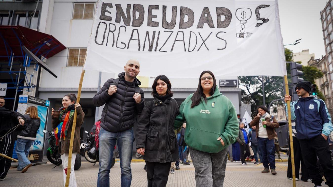 Tres personas frente a un cartel que dice Endeudados Oranizados.