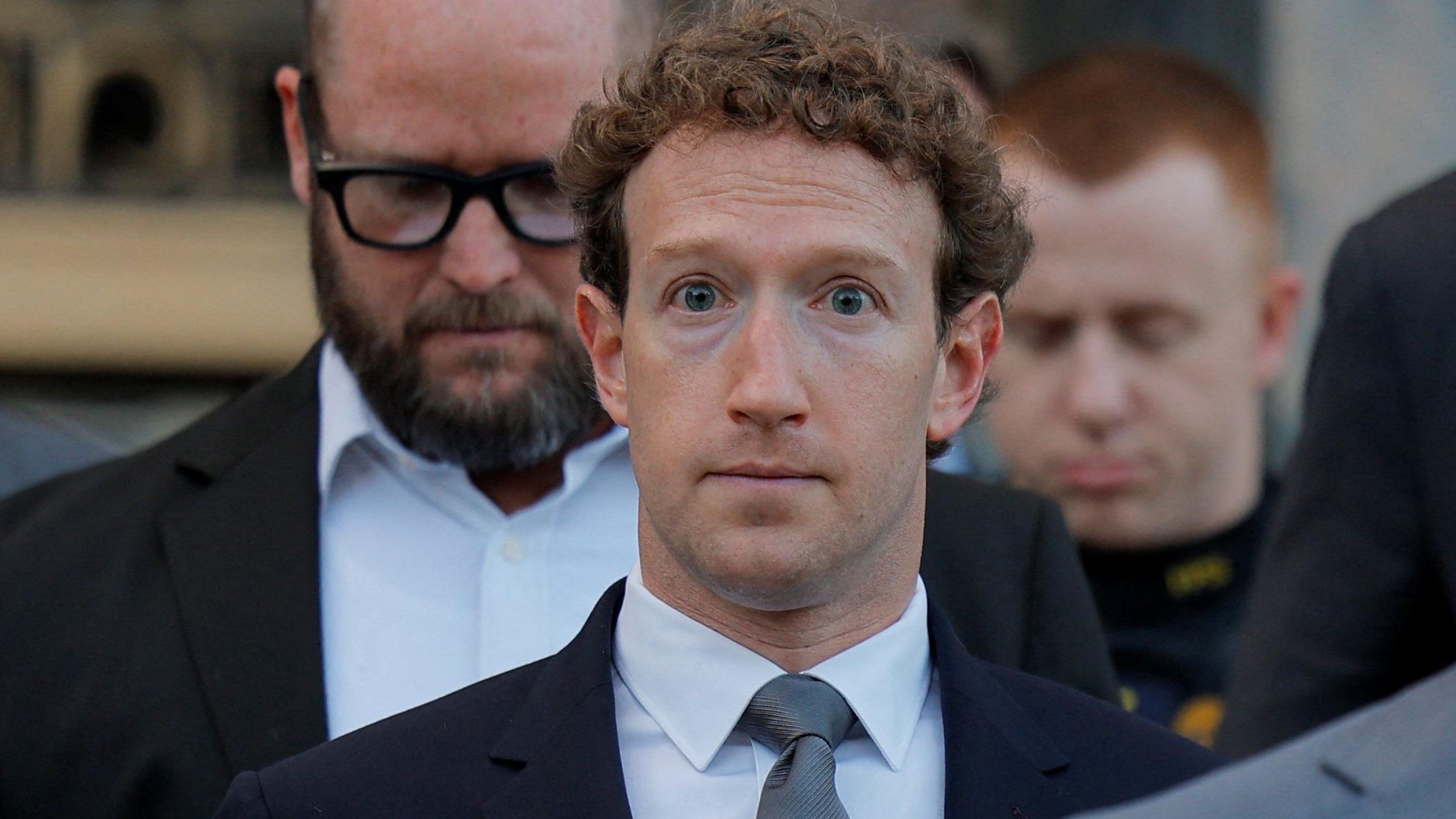 Mark Zuckerberg, rodeado por guardias de seguridad, camina hacia un tribunal de Los Ángeles vestido con un chaqueta azul marino, corbata gris y camisa blanca.