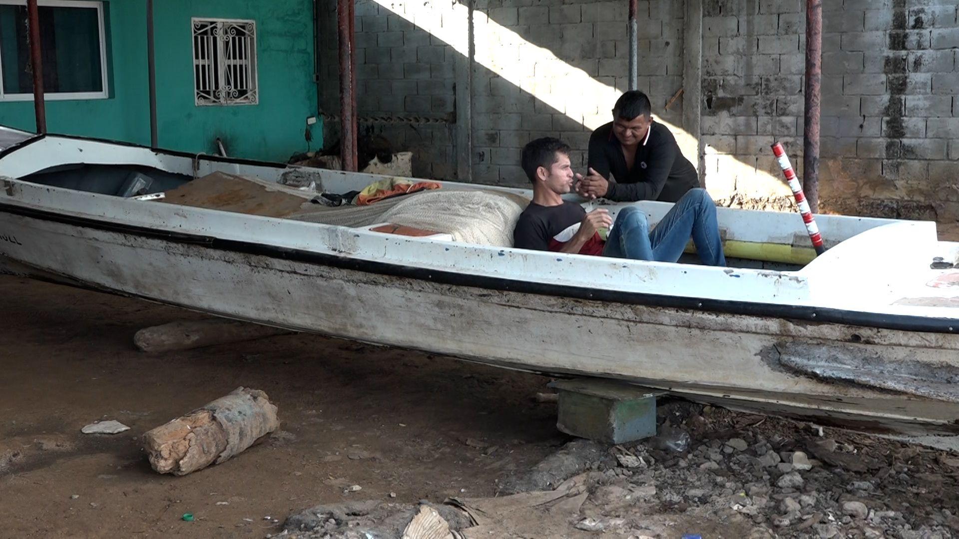 Un hombre dentro de un barco en tierra conversa con otro que está fuera del bote.