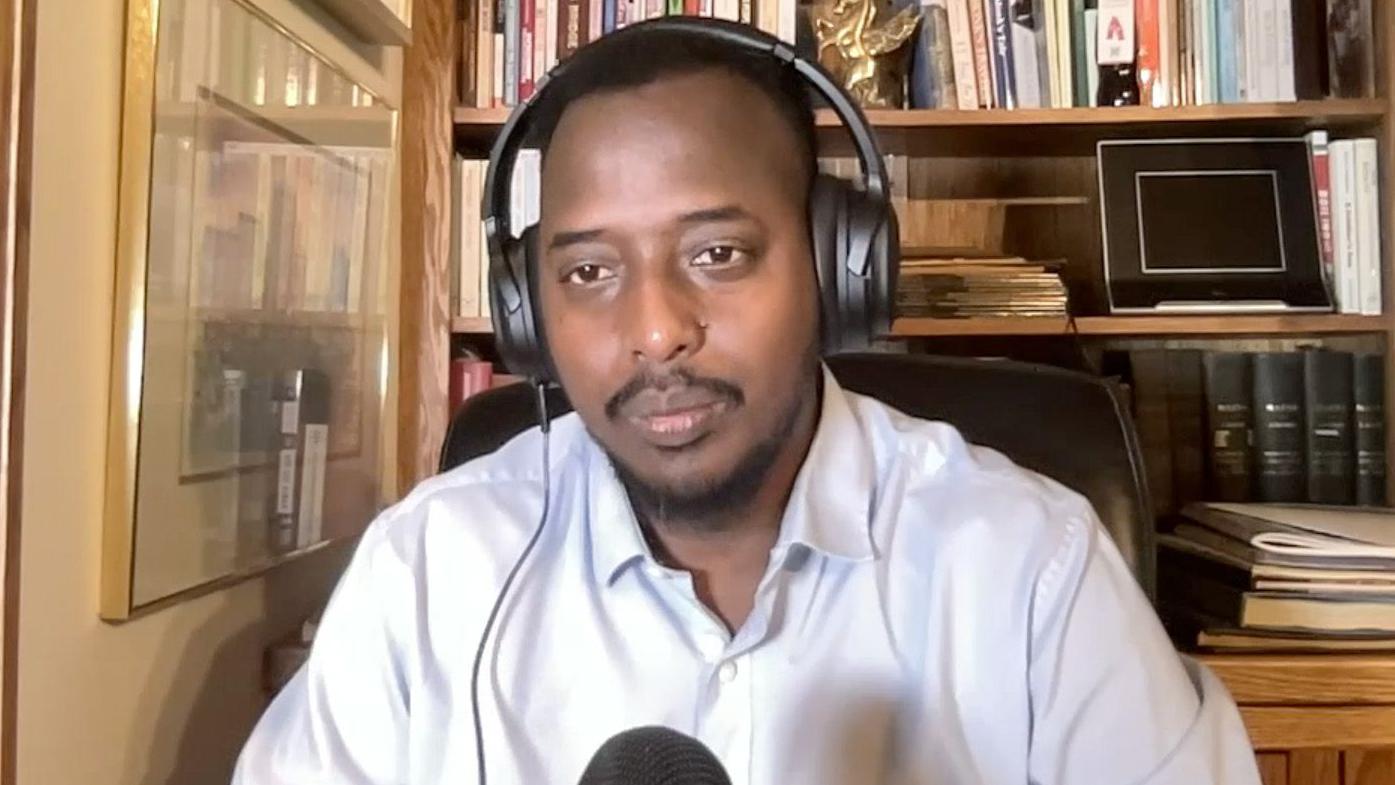 Um homem em um escrit&oacute;rio usa fones de ouvido e fala ao microfone