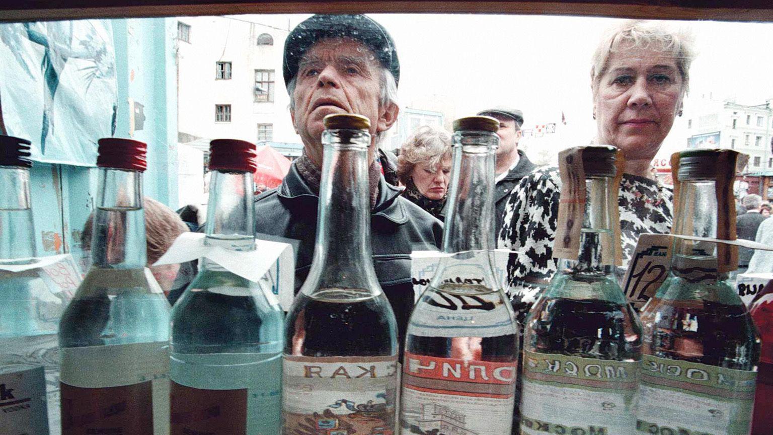 Um homem e uma mulher observam uma banca que vende diversas marcas de vodca em garrafas transparentes.