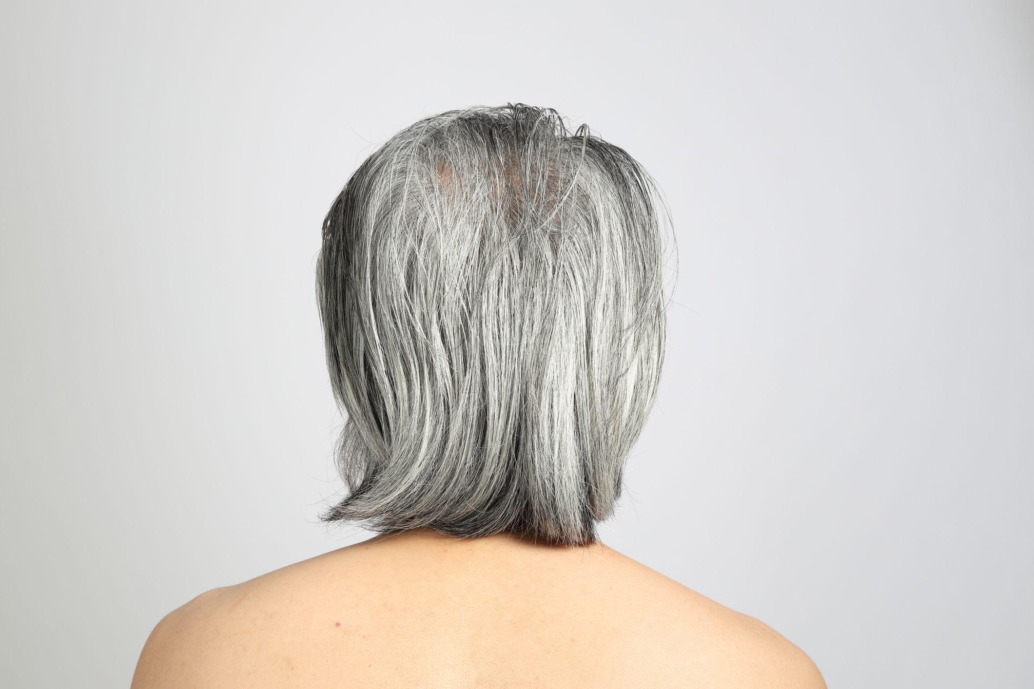 Fotografia de um homem com cabelos grisalhos, visto de costas, contra um fundo branco neutro.