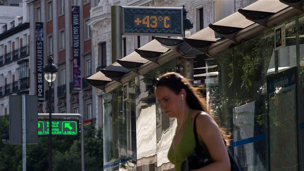 Una mujer en la calle en Madrid pasa frente a un termómetro que indica 43 grados centígrados