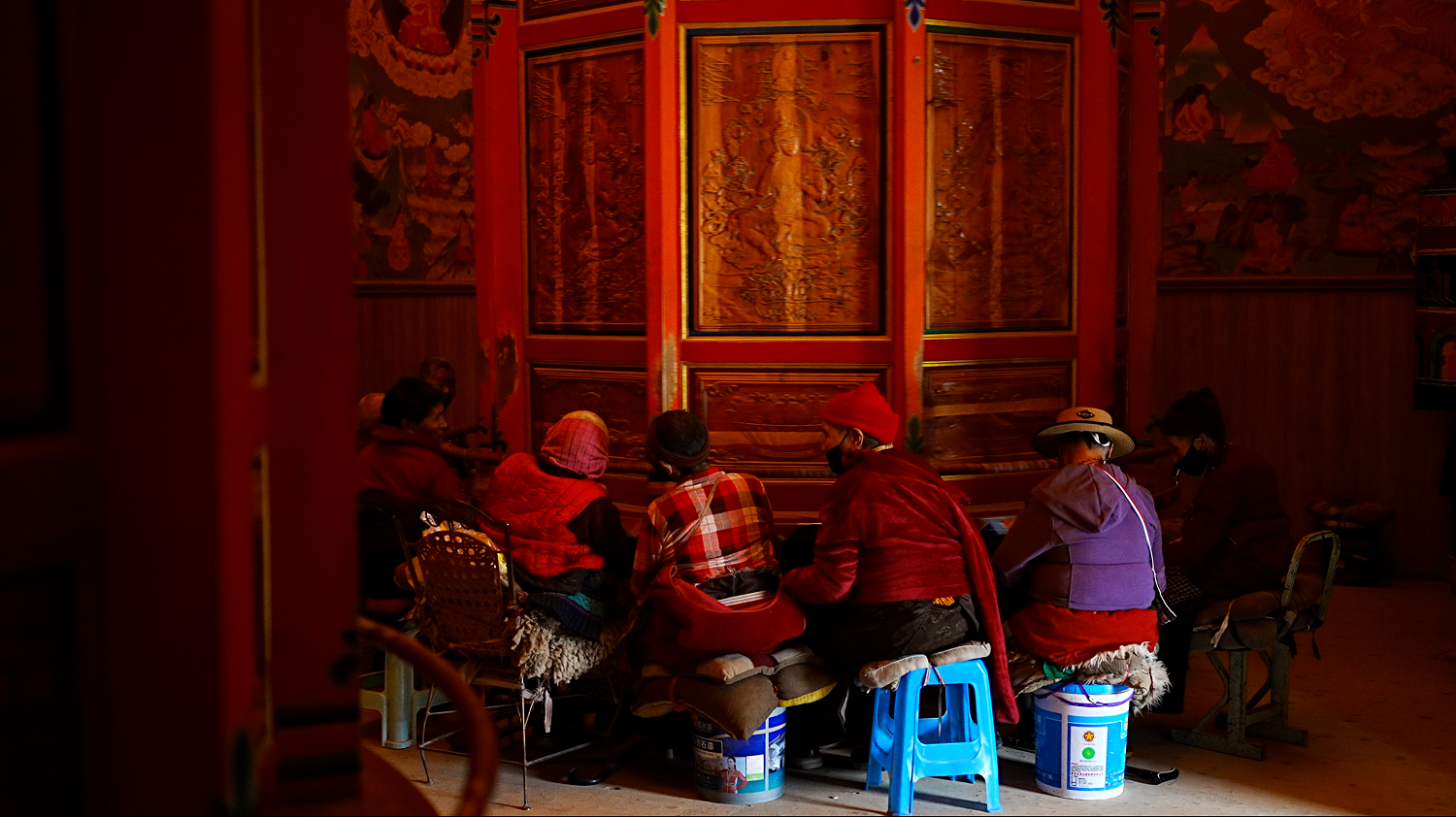 西藏婦女坐在寺廟裡的轉經筒旁