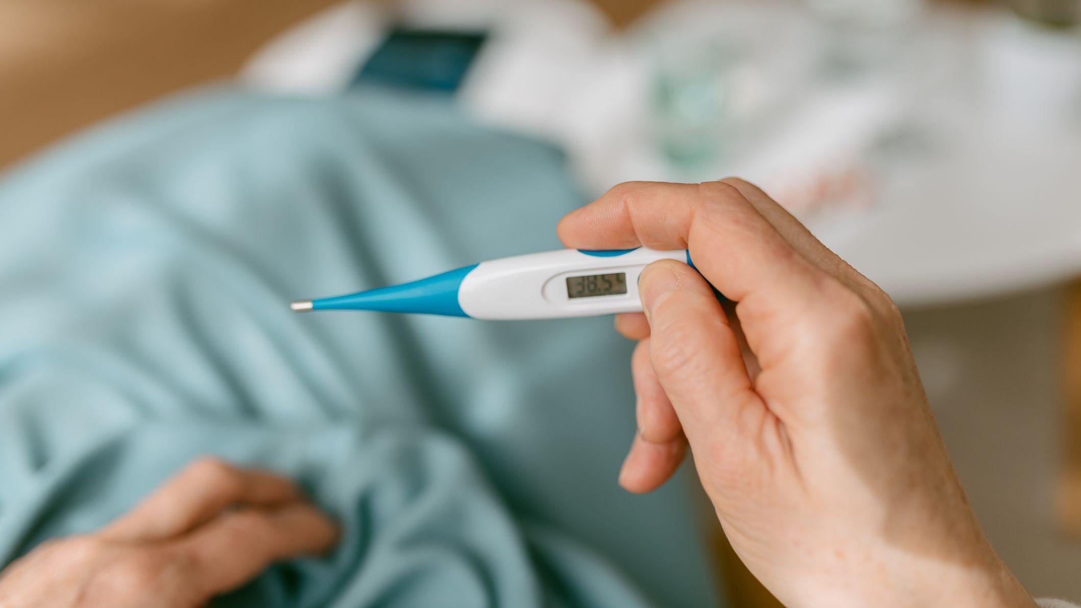 Mão segurando termômetro marcando 38,5 °C