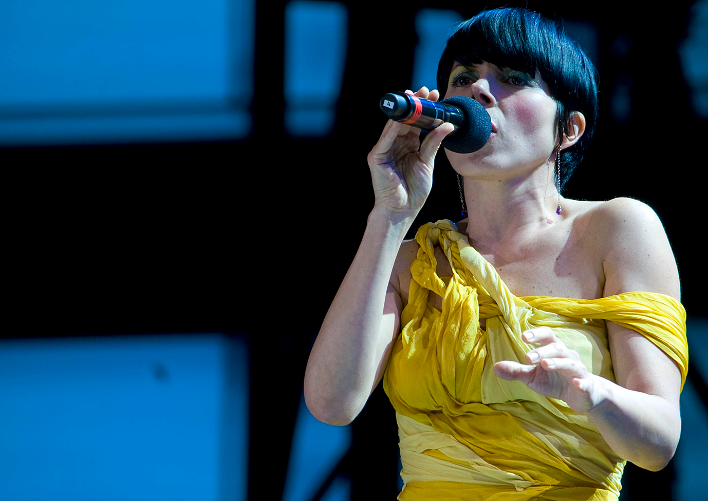 Ely Guerra, vestida con un vestido amarillo, y un micrófono en la mano
