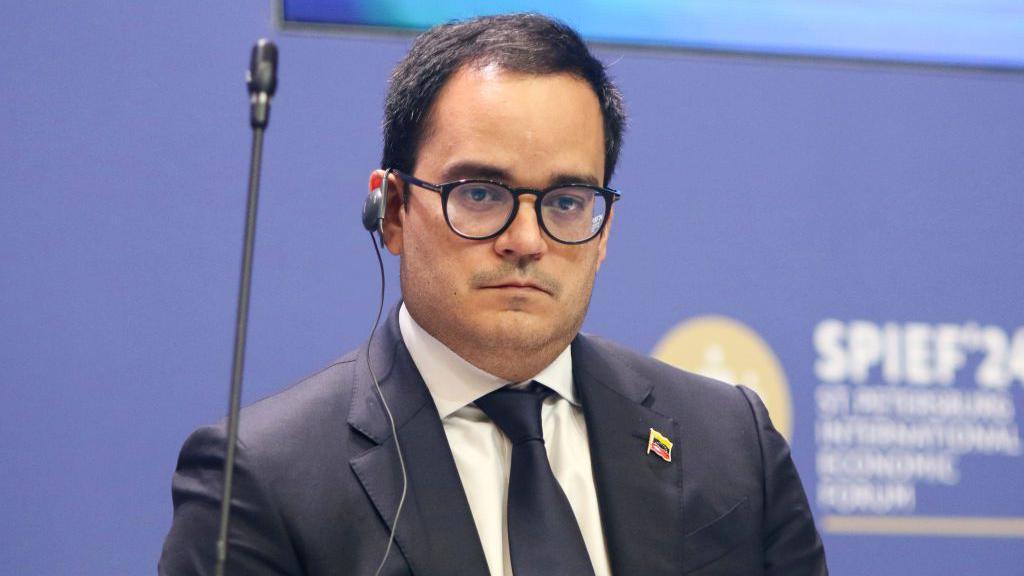 Calixto Ortega S&aacute;nchez, vestido de terno e gravata, com um pin com a bandeira da Venezuela e fone de ouvido