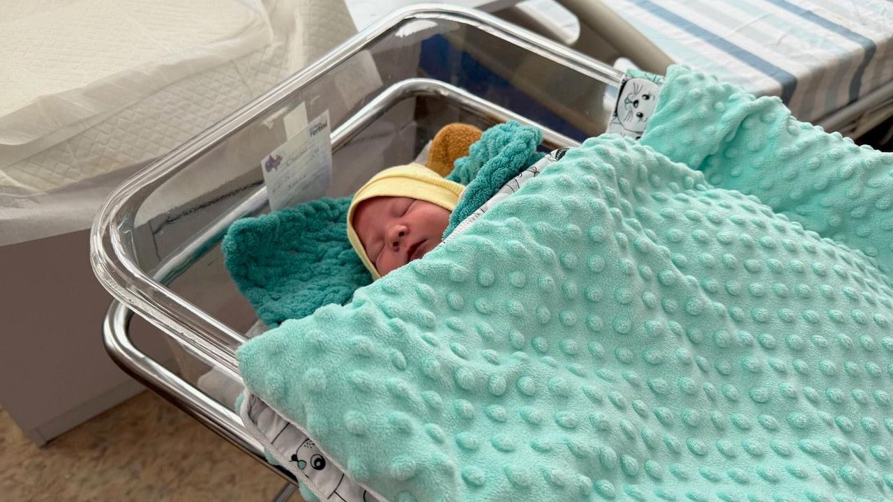 Un bebé dormido con un sombrero amarillo yace en una cama de hospital en Kiyv, bajo una manta verde claro.