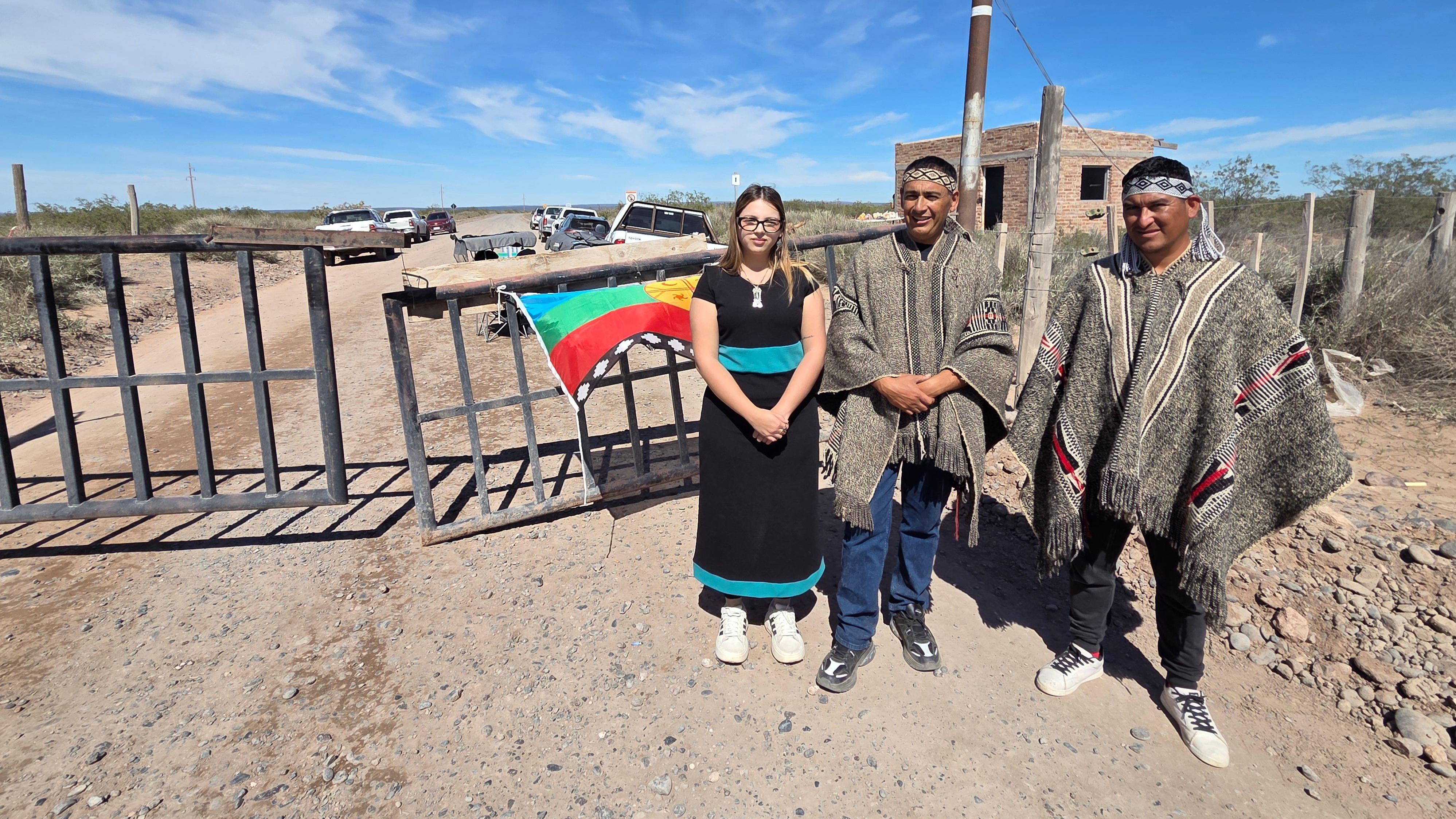 Tres personas paradas frente a una tranquera.