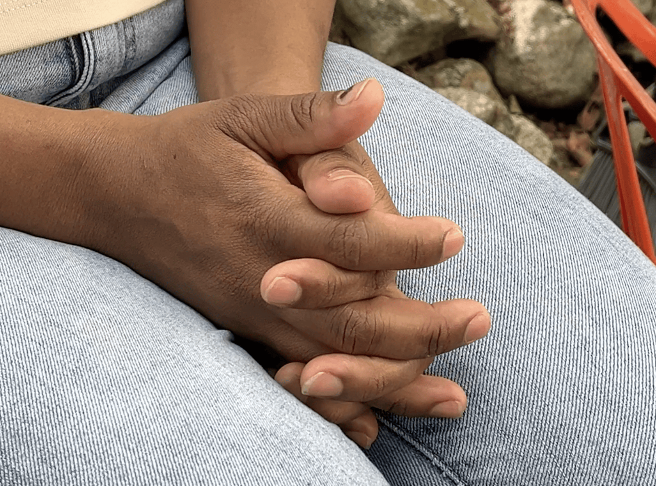 Mãos de Paula sobre as pernas usando calça jeans e uma camisa creme