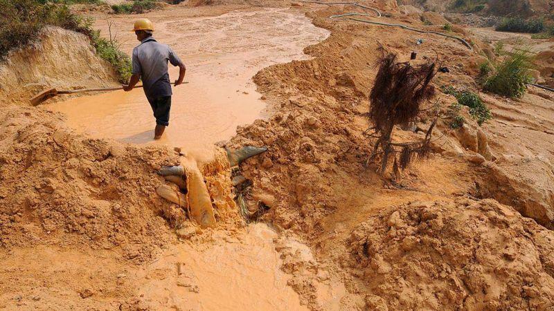 Homem trabalha com rodo na lama, em mina de extração de terras raras na China