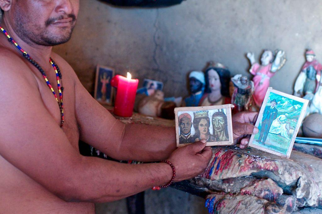 Un santero venezolano sostien en una mano una imagen de unas deidades y en la otra una de José Gregorio.