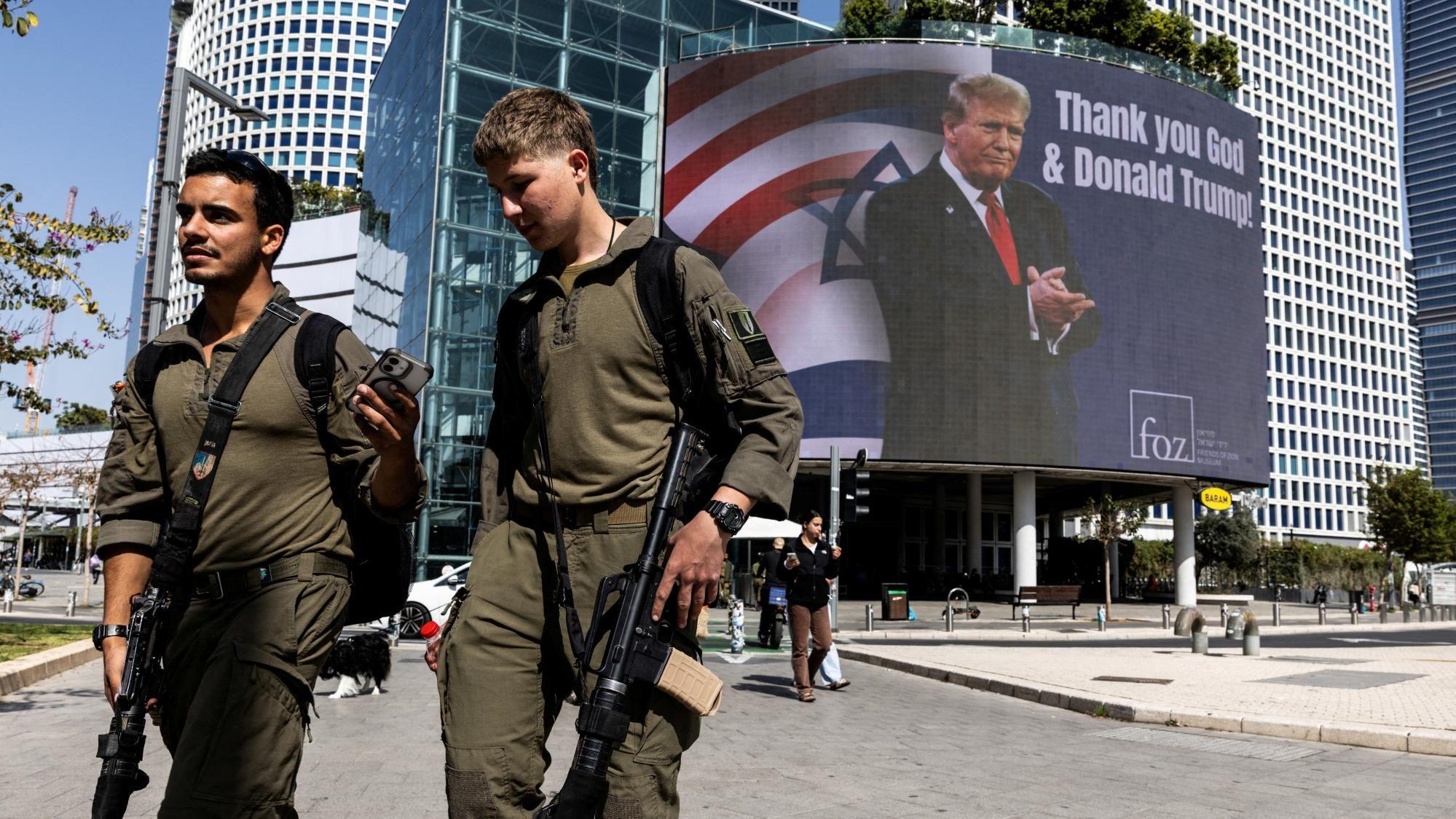 Soldados israelíes pasan junto a una valla publicitaria encargada por un grupo evangélico, en la que aparece una foto del presidente estadounidense Donald Trump con las palabras «Gracias, Dios y Donald Trump», en Tel Aviv, Israel (12 de marzo de 2026)