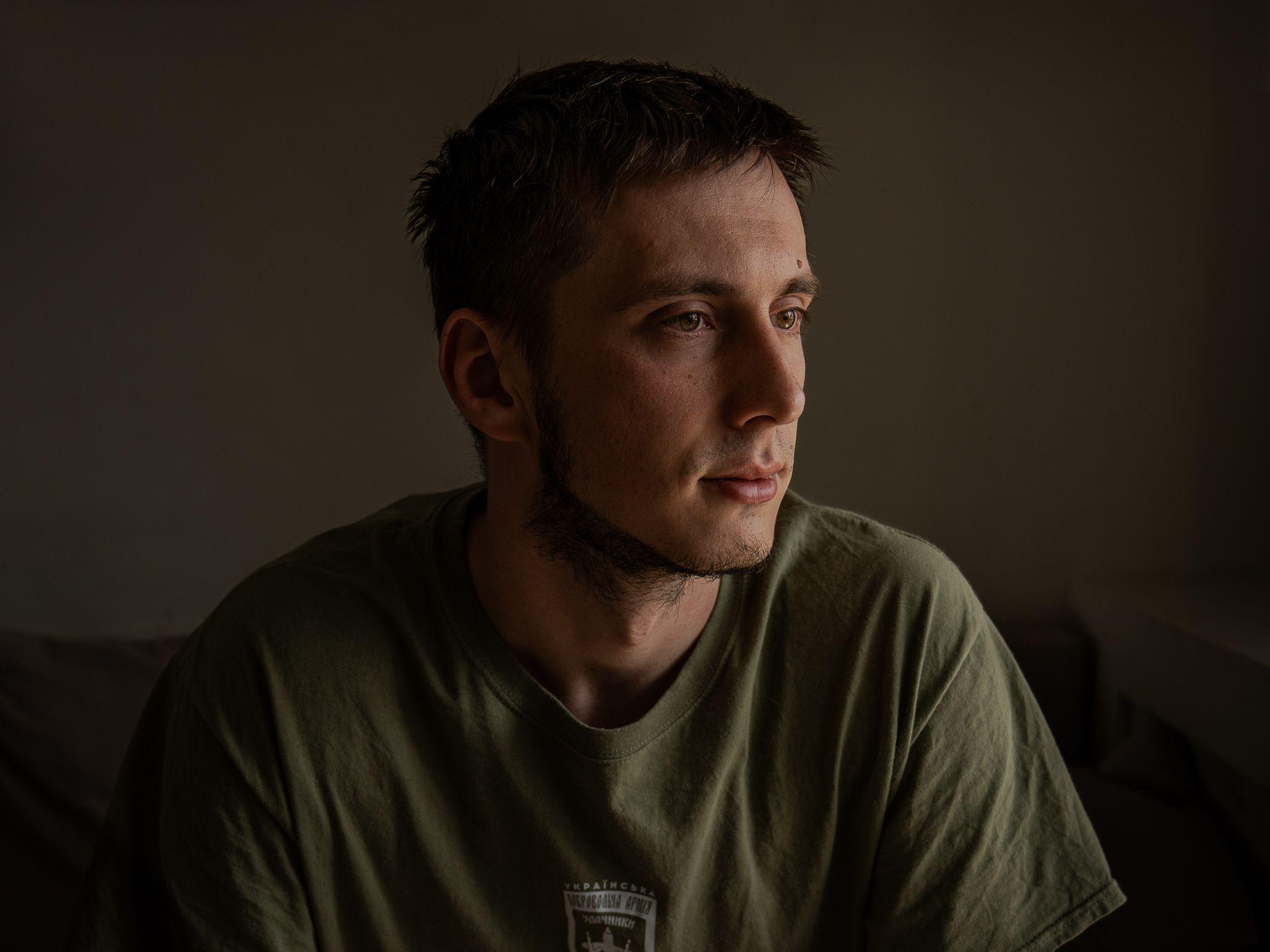 Pavlo, de cabelos escuros e vestindo uma camiseta verde, desvia o olhar da câmera 