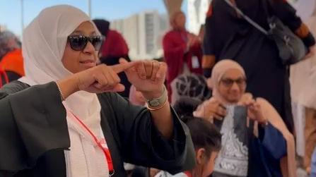 تظهر جاني في مقدمة الصورة إلى اليسار، مرتدية فستاناً أسود وحجاباً أبيض ونظارات شمسية، وتستخدم لغة الإشارة، كما تضع حول عنقها شارة تعريف باللونين الأحمر والأبيض تحمل اسم "الإشارة".