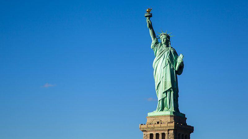 A Estátua da Liberdade, inteira no seu pedestal, em dia ensolarado e sem nuvens no céu