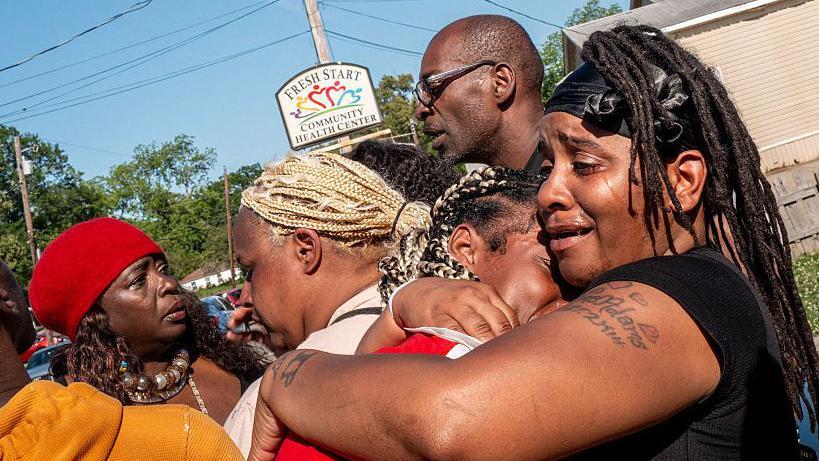 Syrnerica Pugh (a la derecha) recibe consuelo mientras llora la muerte de sus sobrinos y sobrinas. 