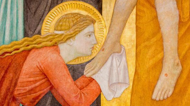 Imagem mostra uma pessoa secando os p&eacute;s de outra