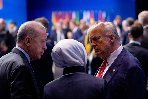 رجلان يرتديان بدلتين رسميتين. أمام أحدهما لافتة كُتب عليها «الولايات المتحدة»، وأمام الآخر لافتة كُتب عليها "الأمين العام لحلف الناتو".