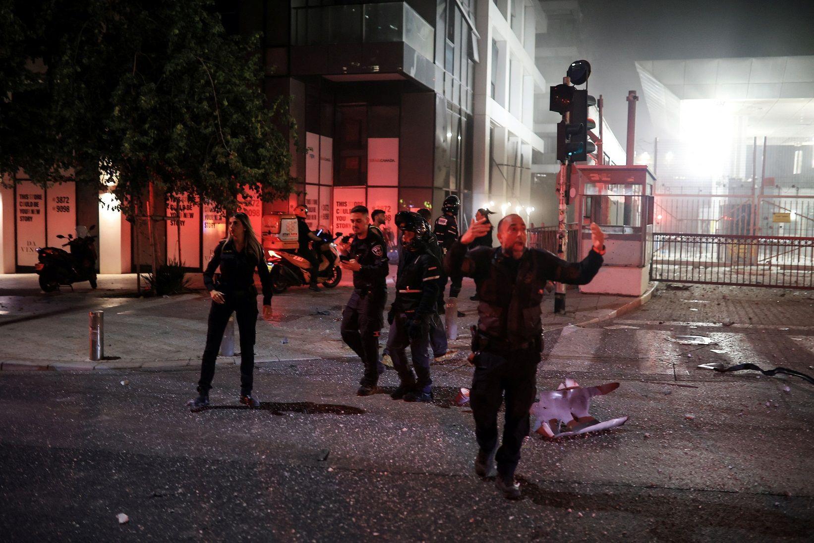 Pessoas na rua à noite em área com destroços; uma das pessoas sinaliza algo com as mãos