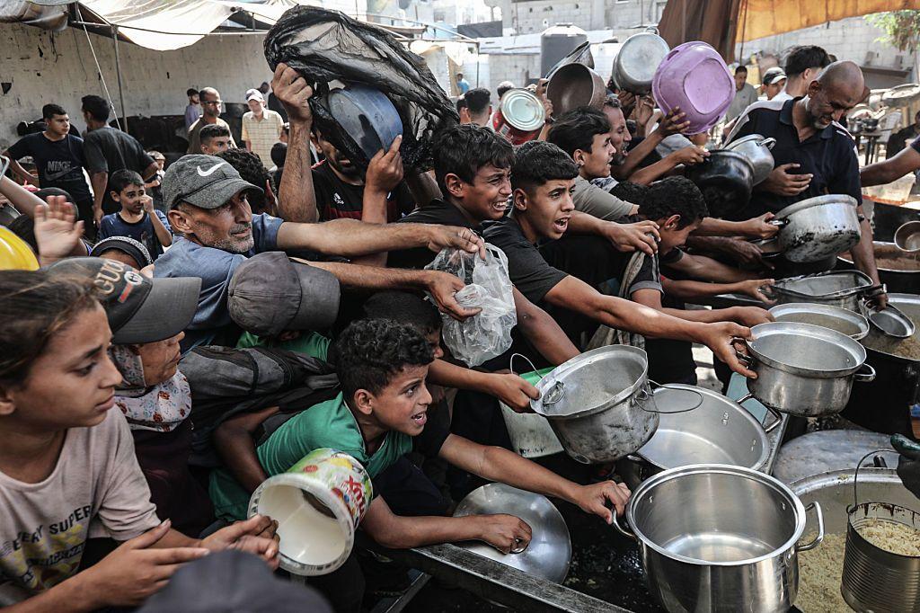 Un grupo de palestinos extiende las ollas que sujetan con la esperanza de recibir comida en un campo de refugiados en el centro de Gaza. 