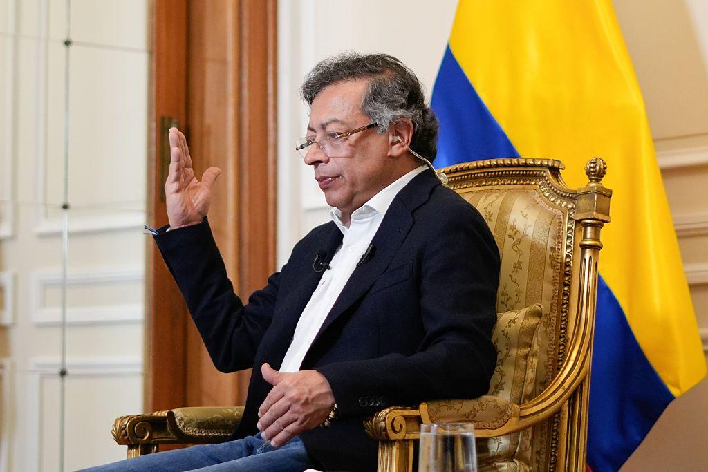 El presidente de Colombia Gustavo Petro, sentado en una silla con bordes dorados y con una bandera colombiana detrás. 