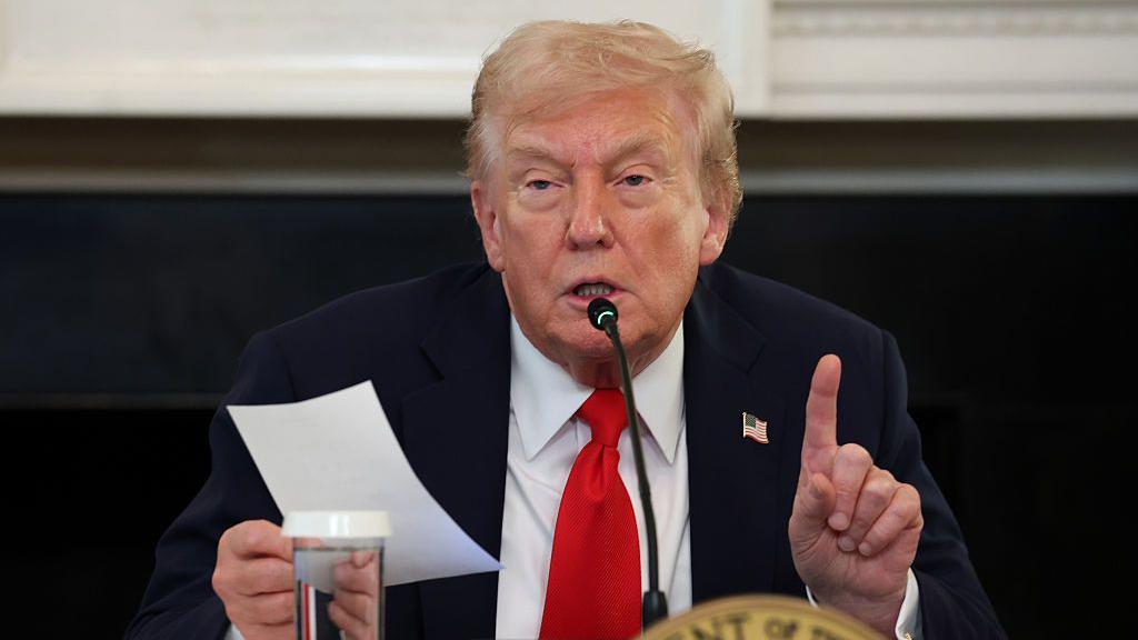 Donald Trump, vestido de traje oscuro y corbata roja, hace declaraciones, sujetando un papel en una mano y con el índice de la otra mano levantado