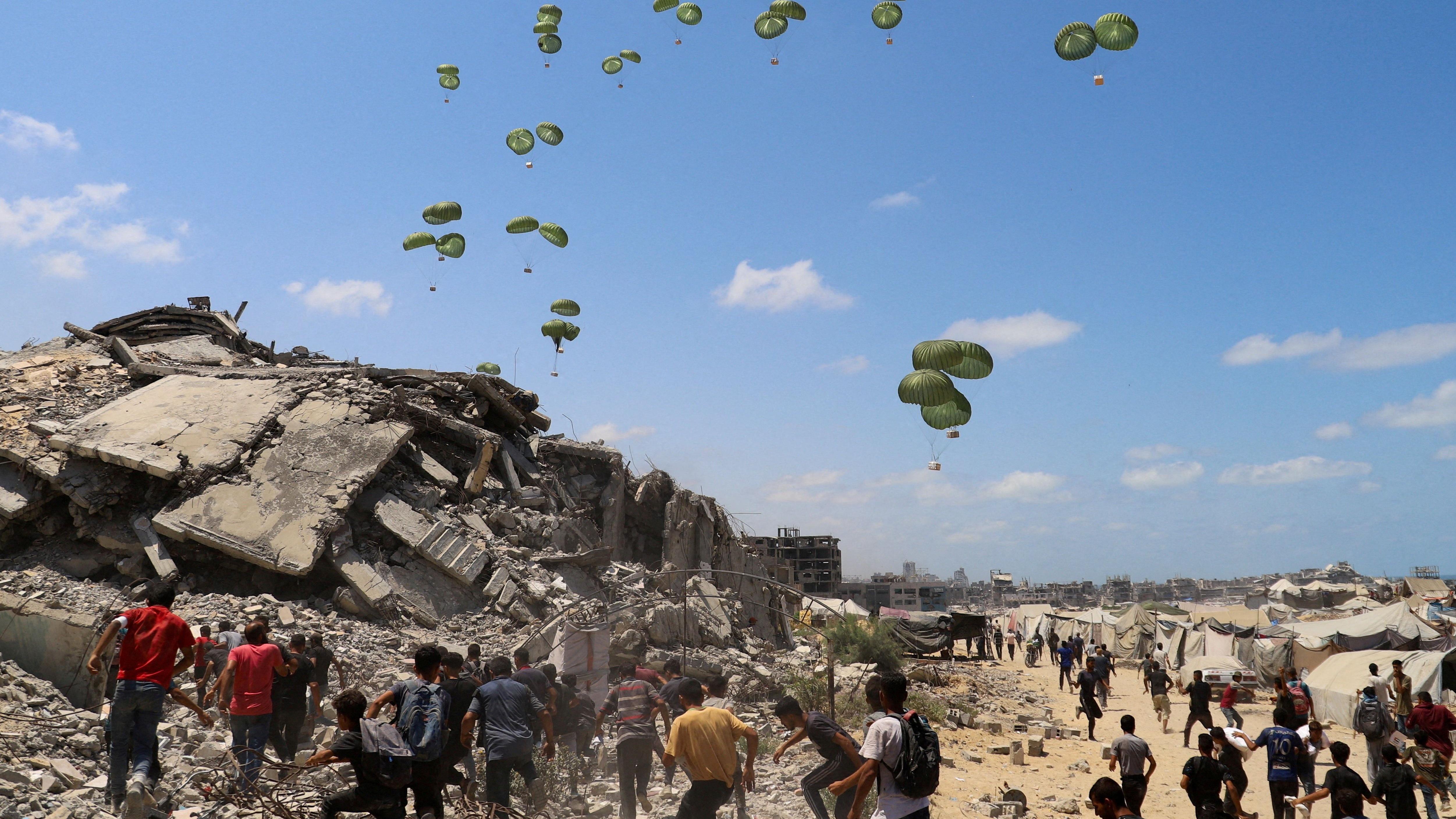 Palestinos correm em direção a paraquedas carregando pacotes de ajuda humanitária lançados de avião sobre o norte da Faixa de Gaza, em 7 de agosto de 2025 