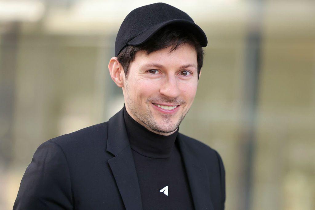 Pavel Durov sonríe y mira a la cámara. Viste un traje negro con una gorra y una camisa de cuello tortuga del mismo color.