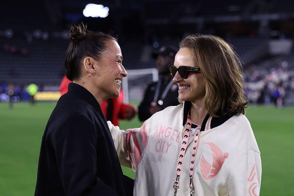 Ali e Natalie sorrindo ao olhar uma para outra em gramado