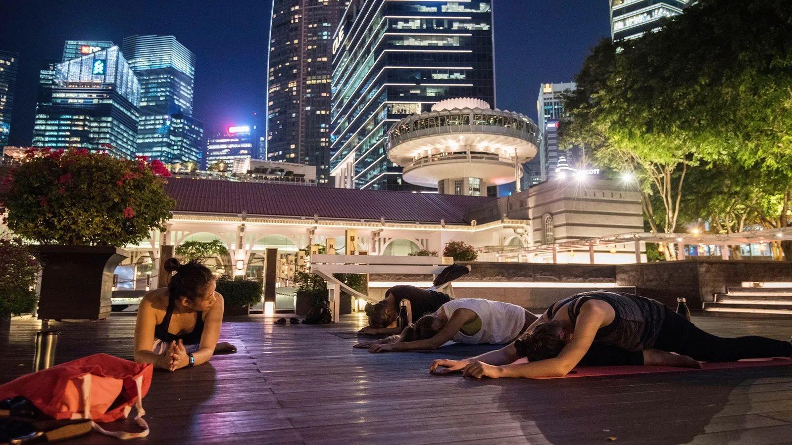 Pessoas fazendo exercício à noite, ao ar livre e em um tapete, em ambiente urbano