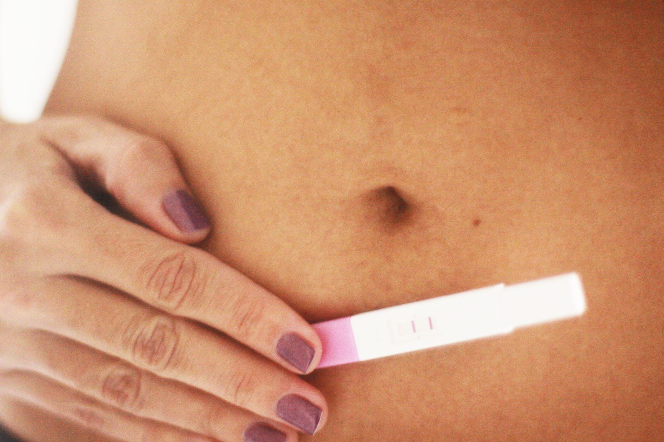 mulher com teste de gravidez positivo encostado em sua barriga