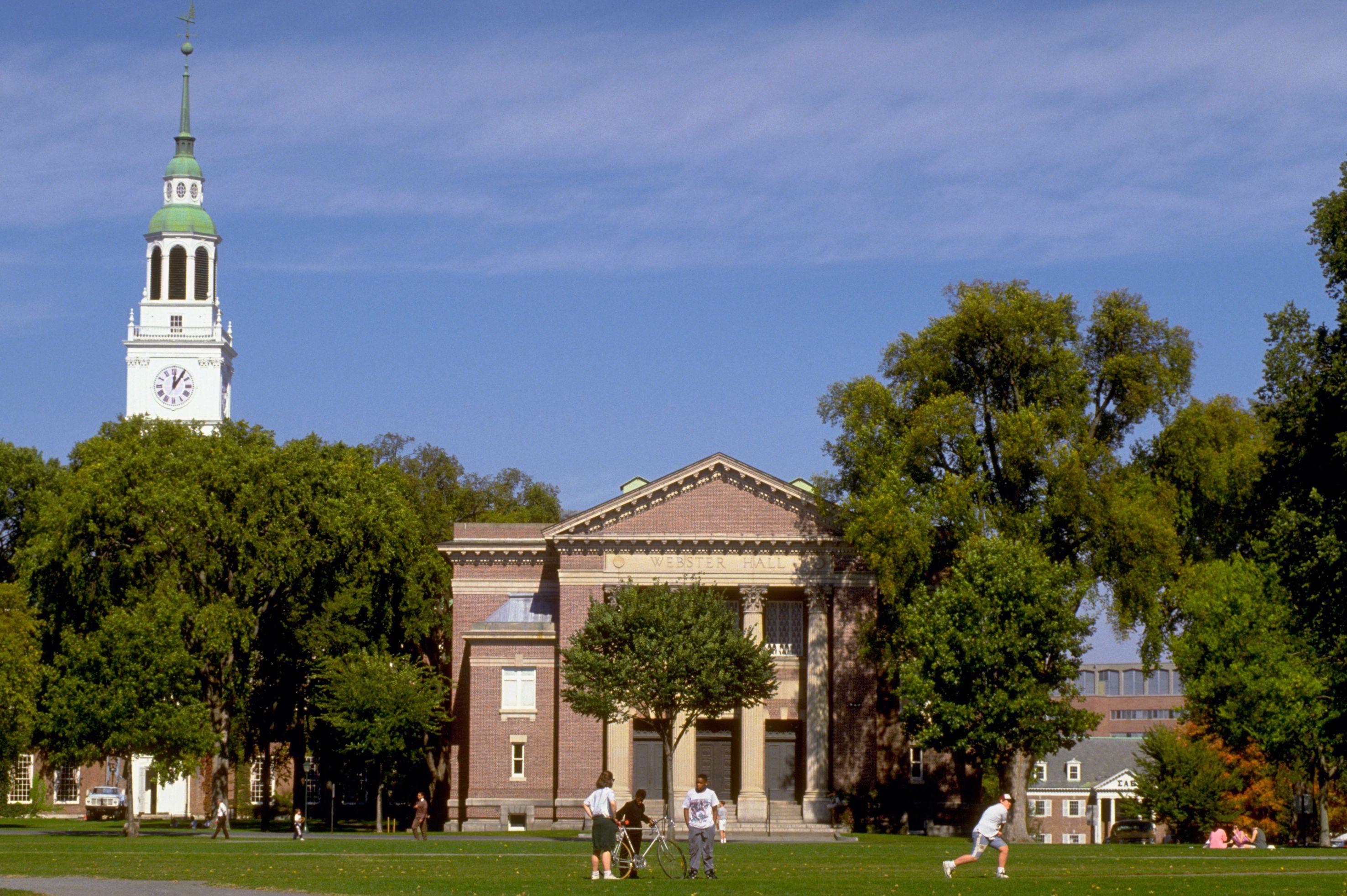 Prédio de faculdade de Dartmouth, nos EUA, rodeada de árvores com folhas verdes e um campo gramado verde, com pessoas andando por esse gramado.