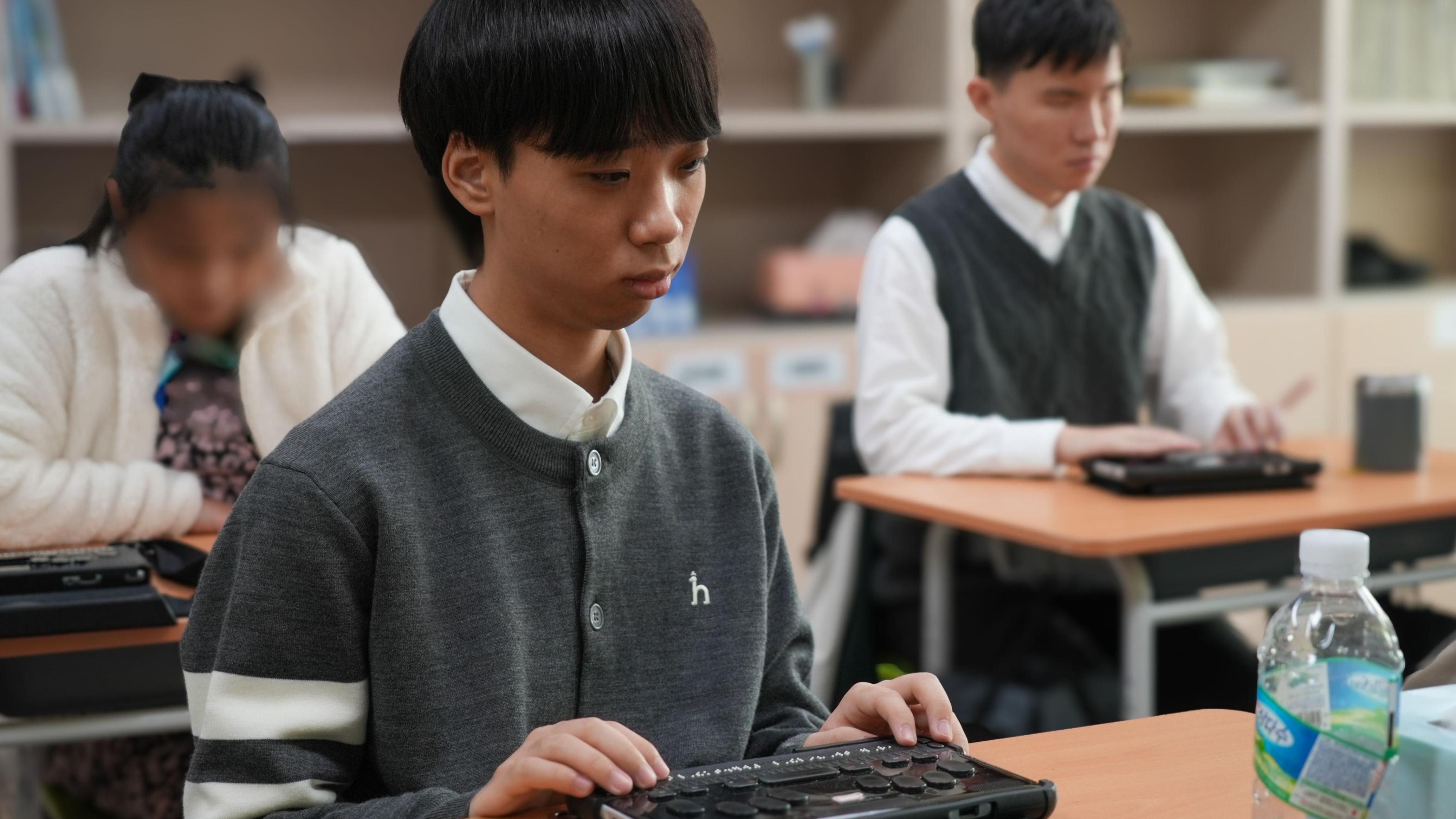 طلاب يجلسون على مكاتبهم وأيديهم على أجهزة عرض برايل