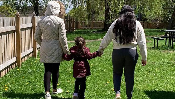Aracely de espaladas con sus dos hijas en un refugio en Buffalo, NY.