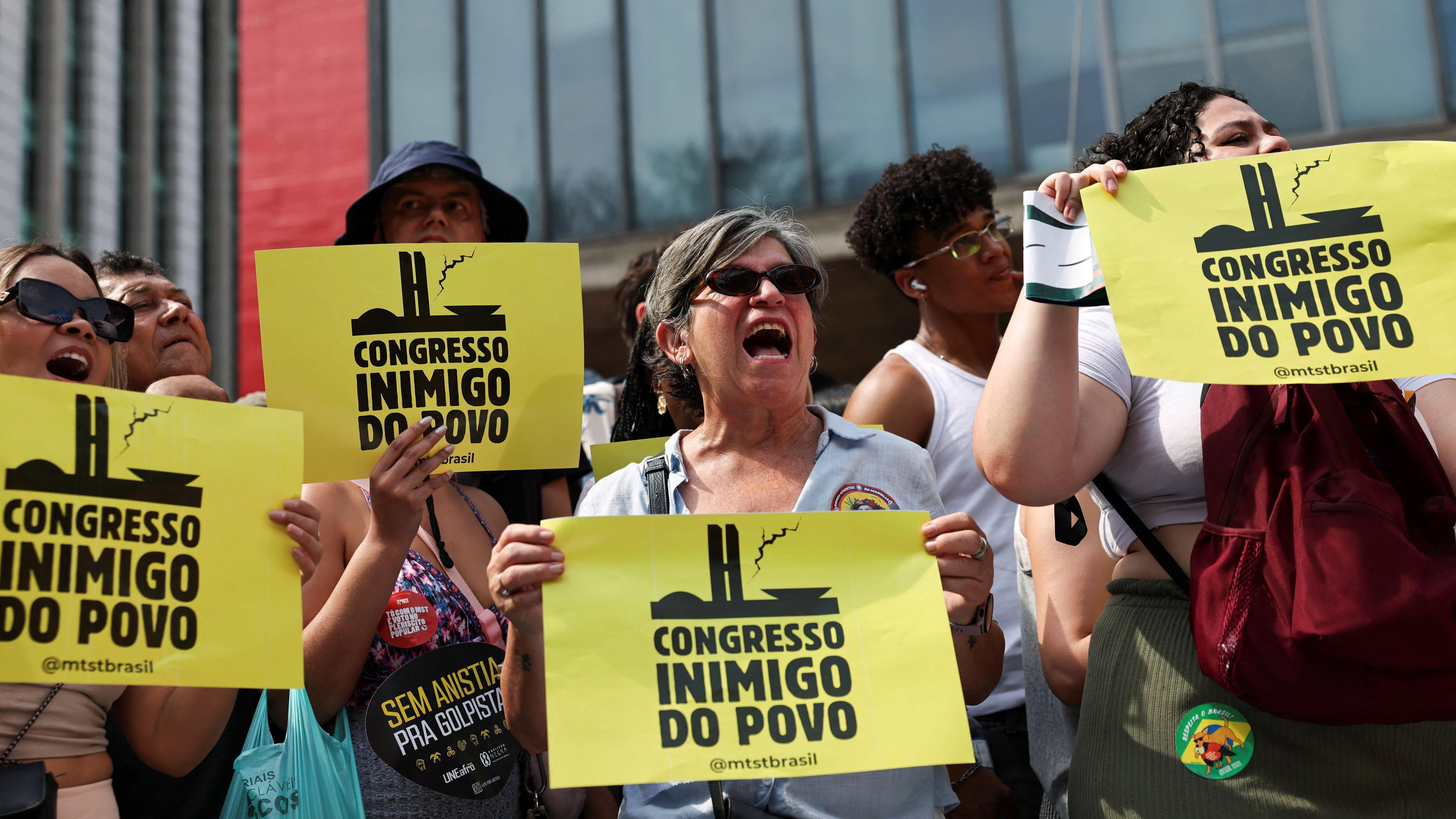 Pessoas seguram cartazes com os dizeres