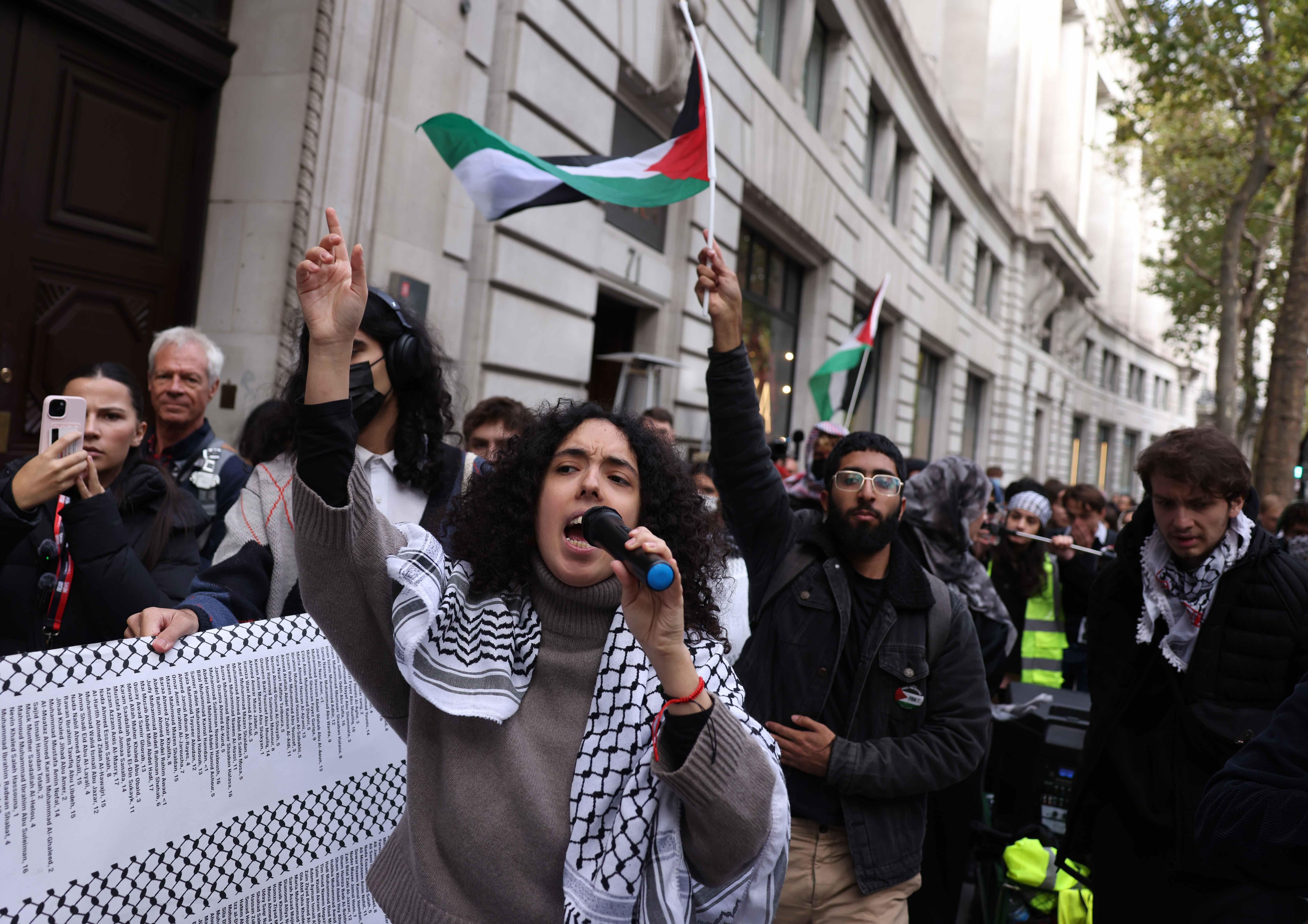 فتاة ترتدي الكوفية الفلسطينية في مظاهرة، وخلفها العلم الفلسطيني