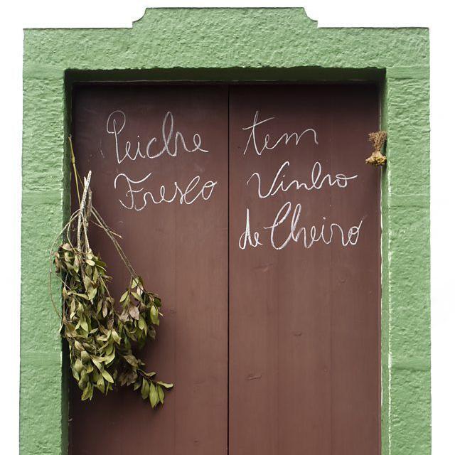 Porta de madeira em parede verde, com um galho e folhas e dizeres em portugu&ecirc;s escritos com giz branco, um deles com erro de ortografia