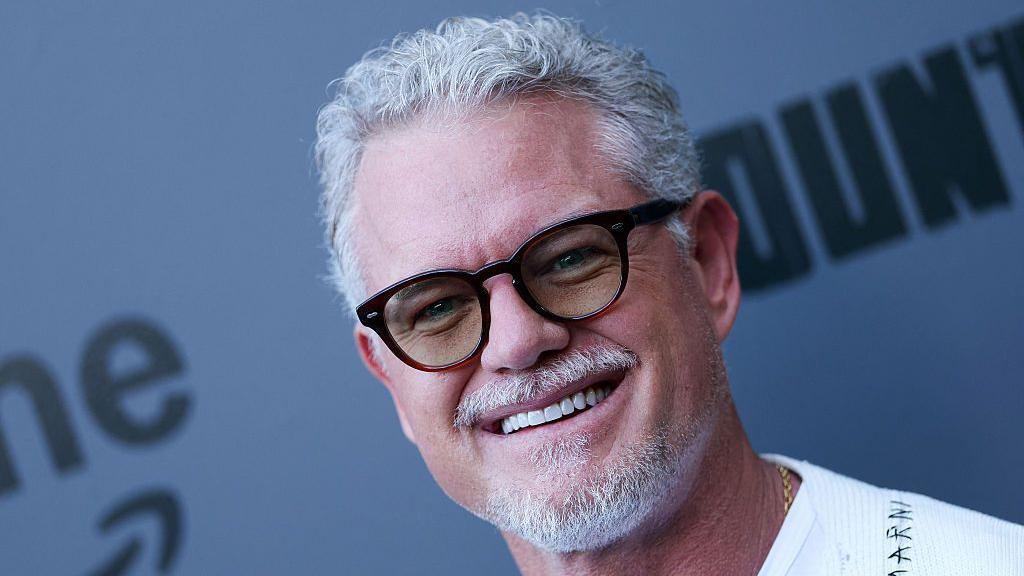 Eric Dane canoso con gafas, sonriendo en un evento.