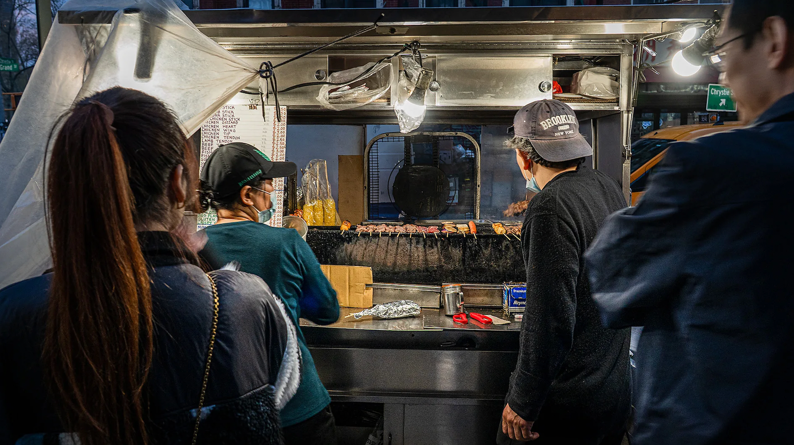 노점 앞에 사람들이 줄을 서 있고, 가게 안에서는 직원들이 꼬치를 굽고 있다.