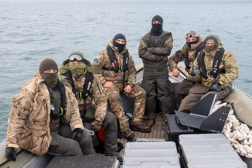 Seis hombres en unifore de camuflaje y con pasamontañas que esconden sus caras, sentados en un barco. El mar Negro se ve en el fondo.