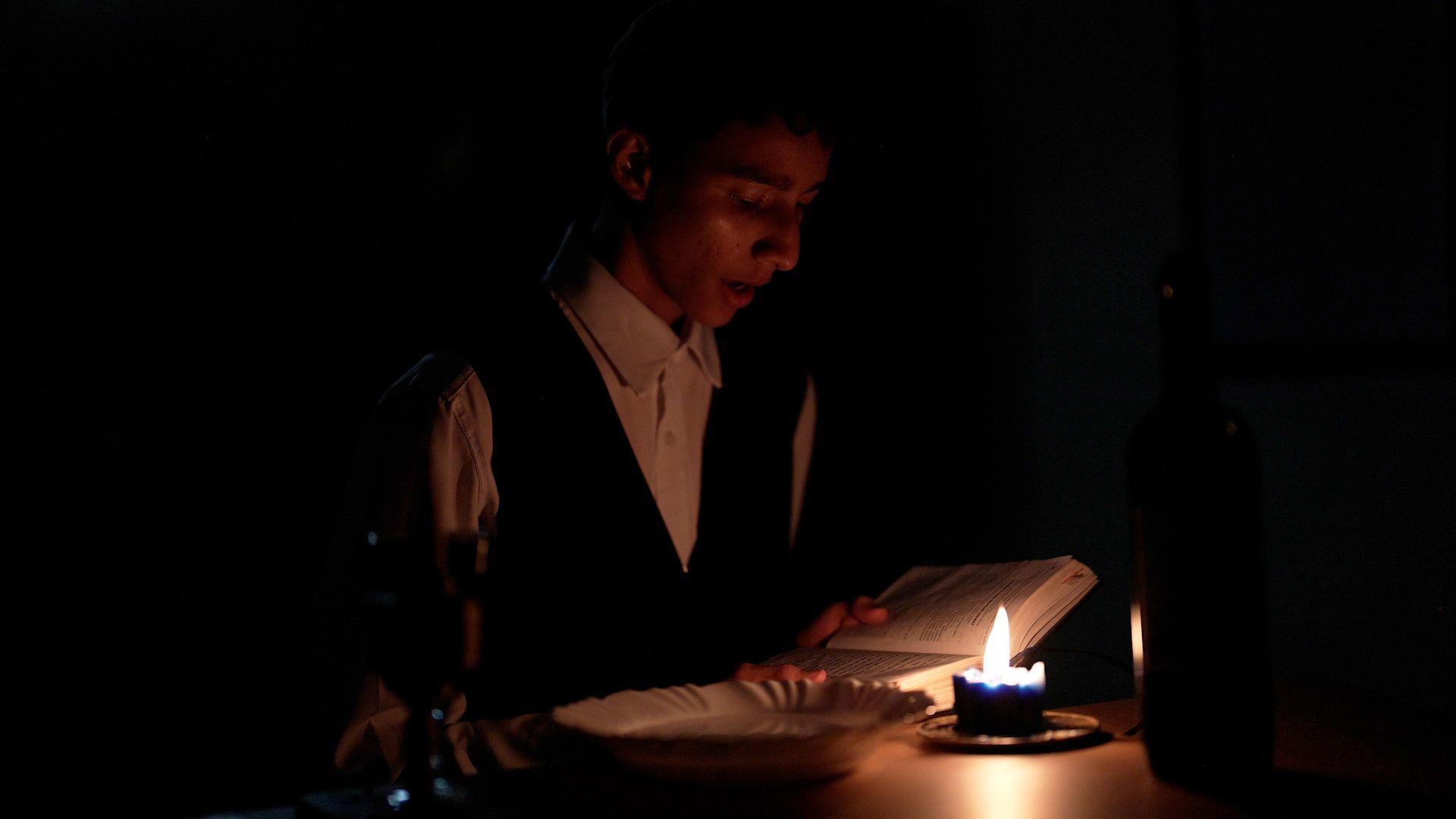 Jovem lê livro religioso à luz de velas