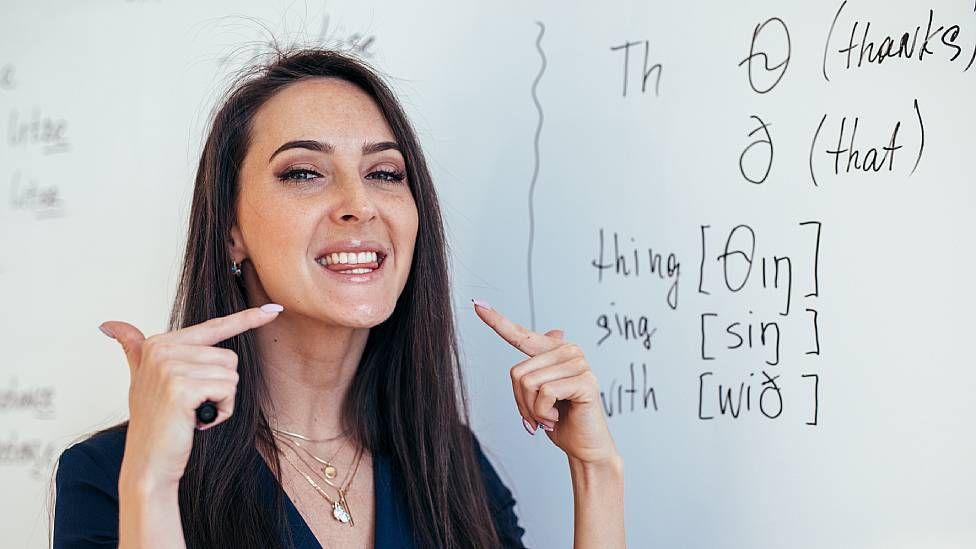 Profesora de inglés enseñando cómo colocar la lengua entre los dientes para realizar un sonido específico